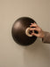 A close-up of a hand adjusting the travertine stone dimmer on the bronzed aluminium shade of the Reverse Wall Lamp.