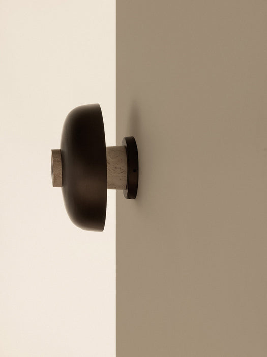 Side view of the Reverse Wall Lamp with its bronzed aluminium shade and travertine base, mounted on the corner of a wall.
