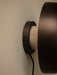 A close-up side view of the Reverse Wall Lamp, detailing its bronzed metal fixture and porous travertine stone base.