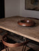 The Rond Bowl in dark wood sits on a rustic wooden table in a dimly lit room, with the back of a chair in the foreground.