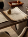 A close-up of a dark wooden desk with a Sentiment Paper Weight on a sketch, a Ready Dining Chair, and a Torso Table Lamp.