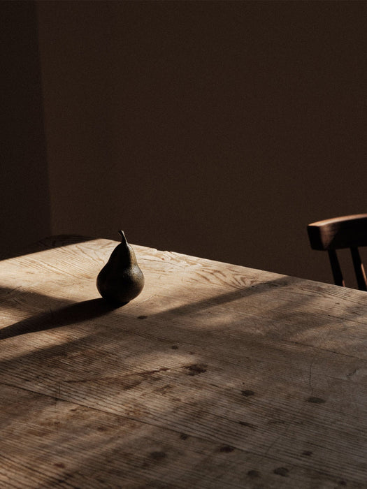 A single pear-shaped Sentiment Paper Weight on a rustic wooden table, with dramatic light from a window casting long shadows.