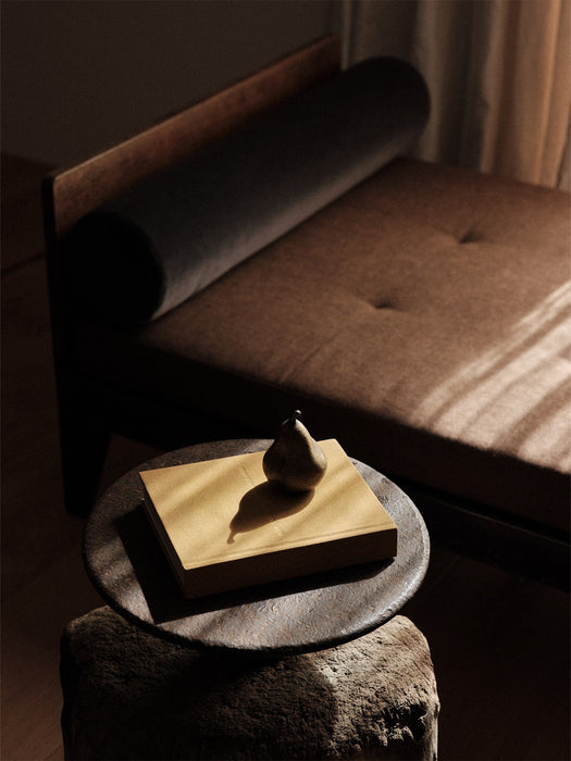 A dark, pear-shaped Sentiment Paper Weight on a yellow book on a rustic side table, with window light creating shadows.