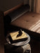 A dark, pear-shaped Sentiment Paper Weight on a yellow book on a rustic side table, with window light creating shadows.