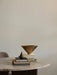 A brass Taper Bowl and a pear-shaped Sentiment Paper Weight are styled on stacks of books on a marble Androgyne Dining Table.