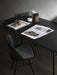 A black Snaregade Oval Table styled with brass cubes, papers and containers, viewed from above with a black dining chair.