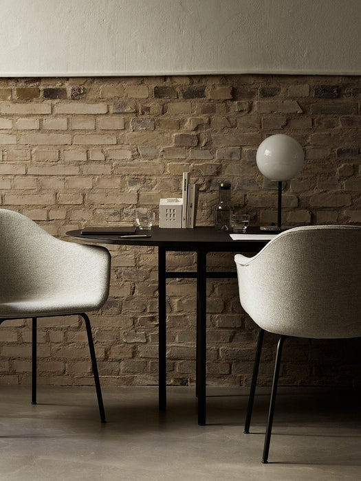 The black Snaregade Oval Table is set for two with light grey Harbour Chairs against an exposed brick wall.