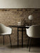 The black Snaregade Oval Table is set for two with light grey Harbour Chairs against an exposed brick wall.