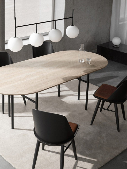 Audo's Snaregade Oval Table in oak with black legs, surrounded by black chairs. A TR Bulb Suspension Frame hangs above.