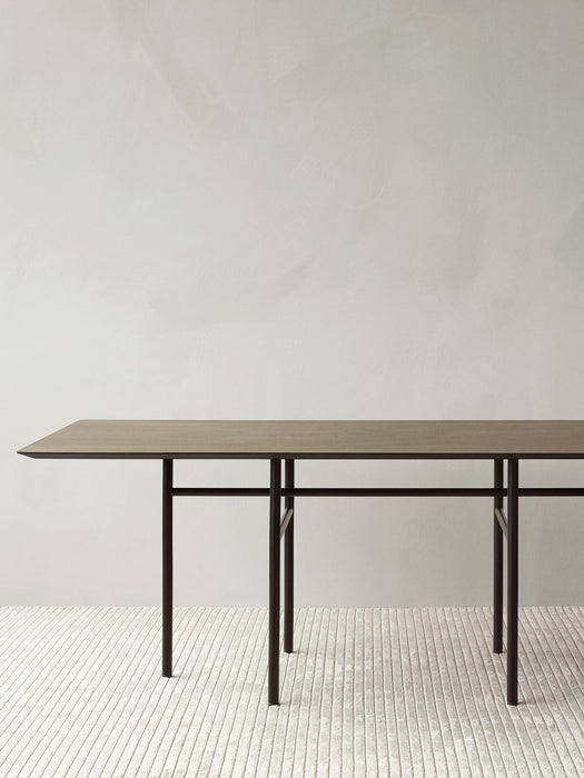 The rectangular Snaregade Dining Table in dark stained oak, seen from the side on a textured Houkime Rug in a bright room.