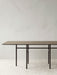 The rectangular Snaregade Dining Table in dark stained oak, seen from the side on a textured Houkime Rug in a bright room.