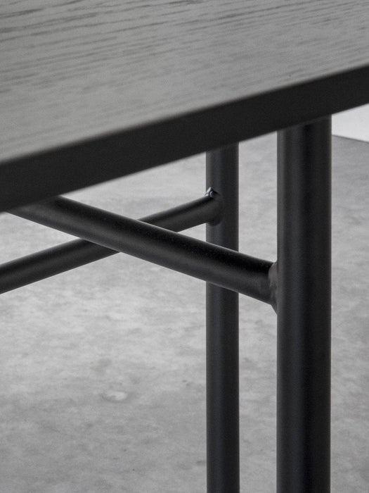A close-up of the Snaregade Dining Table's black steel leg structure under the dark wood tabletop on a concrete floor.