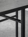 A close-up of the Snaregade Dining Table's black steel leg structure under the dark wood tabletop on a concrete floor.