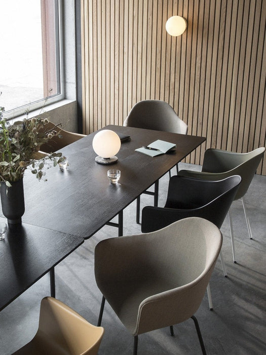 A black Snaregade Dining Table with Harbour Chairs in a modern room with a slatted wooden wall and a TR Bulb on the table.