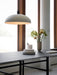 A Hubert Pendant hangs over a black Snaregade Dining Table set with plates and a Cyclades vase with flowers next to a window.