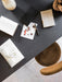 Overhead view of the Snaregade Dining Table styled with stationery, a pen, and books on a dark surface next to a brown chair.