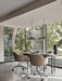 A black Snaregade Dining Table with brown wheeled chairs, set in a room with tiled floors and large windows facing a garden.