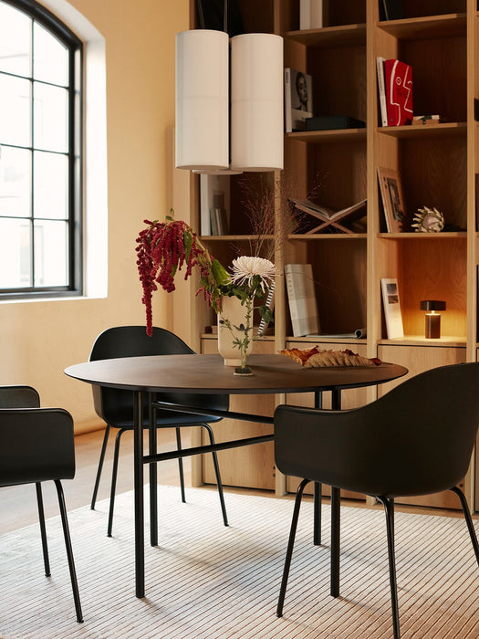 A dining room with a Snaregade Round Table, Harbour Chairs, Hashira Cluster lamp, and a Column Table Lamp on a bookshelf.