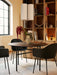 A dining room with a Snaregade Round Table, Harbour Chairs, Hashira Cluster lamp, and a Column Table Lamp on a bookshelf.
