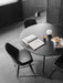 A black, round Snaregade Dining Table and Synnes Chairs styled with books and accessories in a dark, minimalist interior.