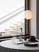 A view of the round Snaregade Dining Table set with dark plates and glassware under a glowing spherical pendant light.