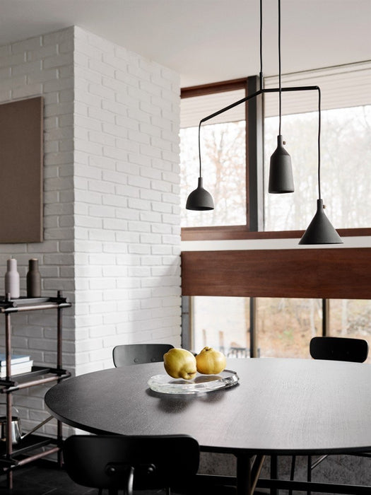 The round, black Snaregade Dining Table set for dining under a pendant light in a room with a white brick wall and chairs.