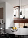 The round, black Snaregade Dining Table set for dining under a pendant light in a room with a white brick wall and chairs.