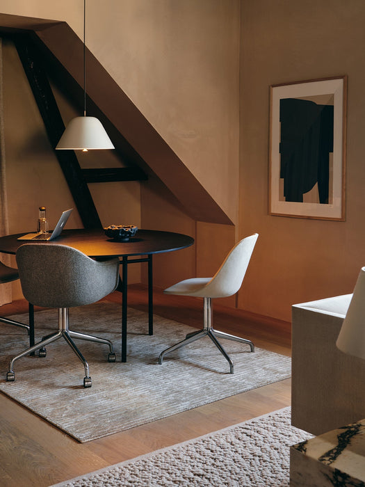 A warmly lit room with a round Snaregade Dining Table, Harbour Dining Chairs, and a white Levitate Pendant lamp.