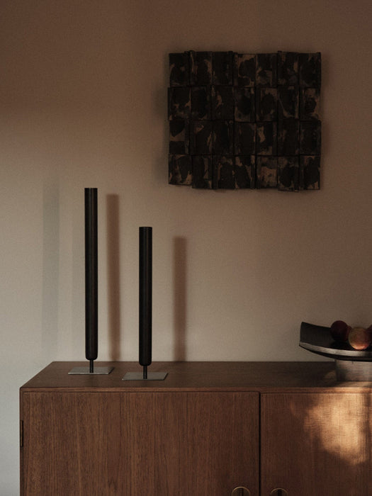A lifestyle image of two black Stance Vases and a Relevé Platter on a wooden sideboard, with dark textured art on the wall.