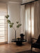 A black Stance Vase with a green branch, a gold Taper Bowl, and a black Surround Vase on a coffee table in a sunlit room.