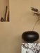 The dark brown Surround Vase holding a single branch, styled on a Calacatta Viola marble Plinth Pedestal by a wall shelf.