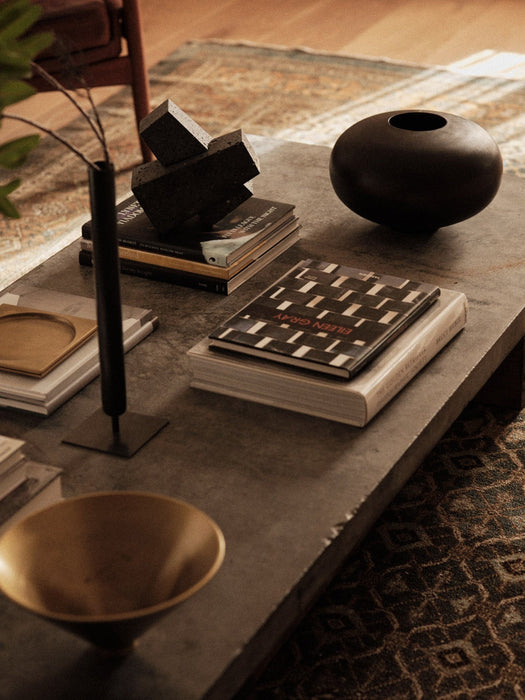 A dark stone coffee table styled with Stance Vase, Converge Book Ends, Surround Vase, and Taper Bowl amongst books.