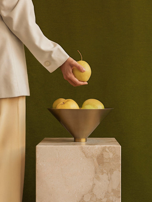 A person in a cream blazer places a yellow pear into the Audo Taper Bowl, which is filled with pears and on a Plinth Tall.