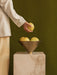 A person in a cream blazer places a yellow pear into the Audo Taper Bowl, which is filled with pears and on a Plinth Tall.