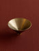 Overhead view of the Audo Taper Bowl in brushed brass. The cone-shaped bowl rests on a textured, deep red surface.