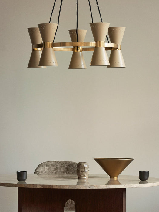 A beige Collector 5 Pendant lamp hangs above a marble-topped Androgyne Dining Table, which holds a brass Taper Bowl.