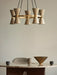 A beige Collector 5 Pendant lamp hangs above a marble-topped Androgyne Dining Table, which holds a brass Taper Bowl.
