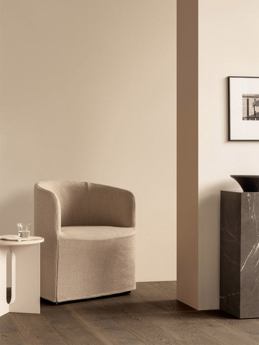 The Tearoom Club Chair in a sandy loose cover, placed next to a white Androgyne Side Table and a tall, dark marble Plinth.