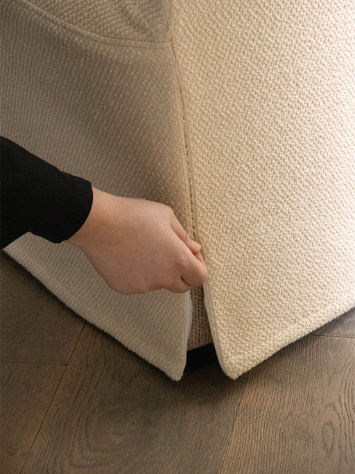 A close-up of a hand pulling at the seam of the textured, light-coloured loose cover on the base of the Tearoom Club Chair.