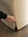 A close-up of a hand pulling at the seam of the textured, light-coloured loose cover on the base of the Tearoom Club Chair.