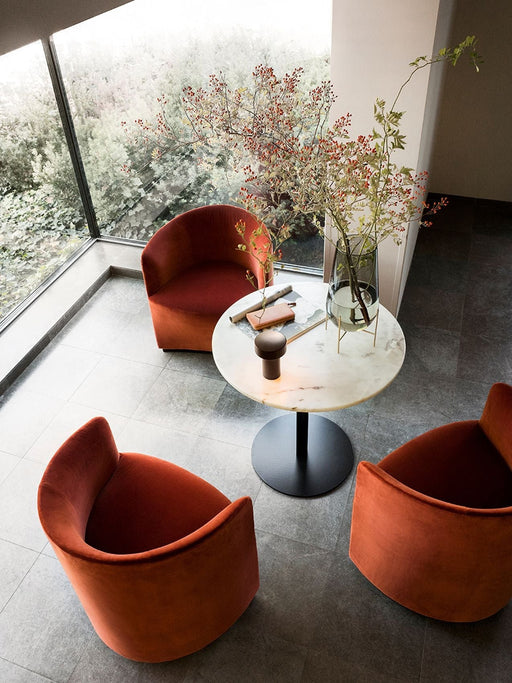 Three rust-coloured velvet Tearoom Club Chairs around a marble cafe table by a large window overlooking a garden.