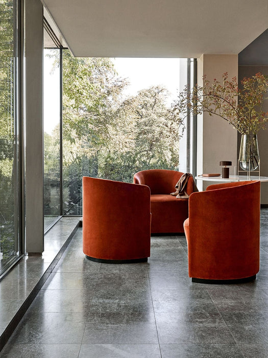 Three rust-coloured velvet Tearoom Club Chairs in a minimalist room with floor-to-ceiling windows overlooking a lush garden.