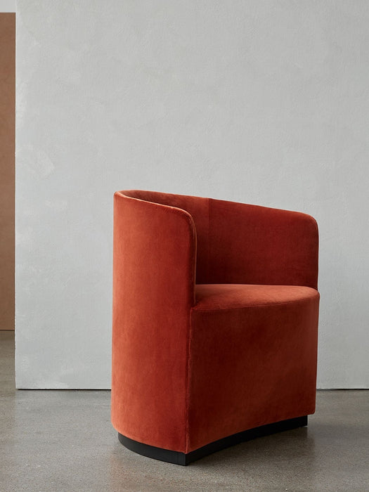 Tearoom Club Chair upholstered in burnt orange velvet, shown from a three-quarter view against a pale grey concrete wall.