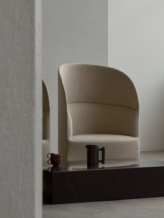 A beige Tearoom Lounge Chair, High Back, sits behind a black marble Plinth table with a Yana Brewing Pot and two cups.