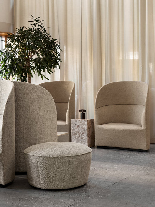 A lounge setting with several sand-coloured Tearoom Lounge Chairs and a Cairn Pouf by a marble Plinth Cubic side table.