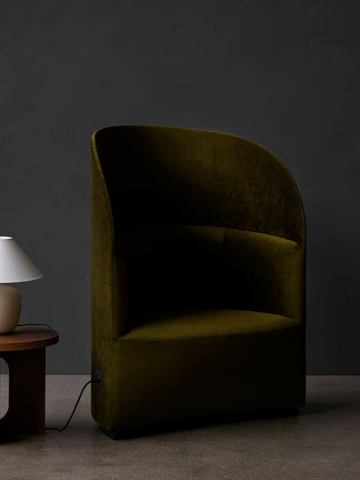 A green velvet Tearoom Lounge Chair with a high back, shown with its power outlet, next to a wooden Androgyne Side Table.