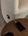 A close-up of the Tearoom Lounge Chair's built-in USB port, with a cable charging a phone on a wooden Androgyne Side Table.
