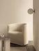 A cream Tearoom Lounge Chair with Loose Cover next to an Androgyne Side Table in a neutral room with a TR Bulb Wall Lamp.