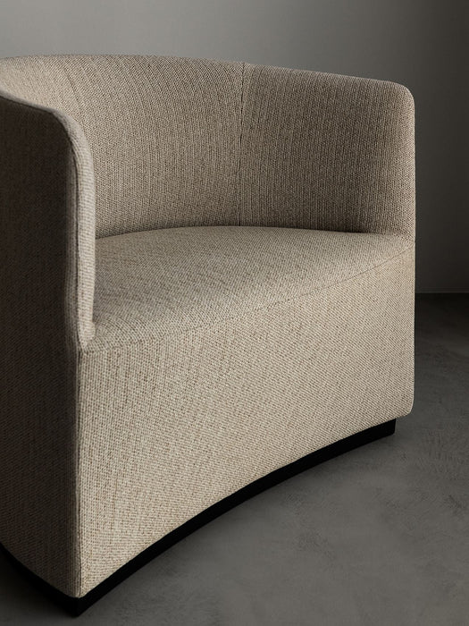 Close-up of the Tearoom Lounge Chair in light beige textured fabric, showing its curved back and armrest against a grey wall