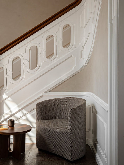 Tearoom Lounge Chair in patterned fabric, sitting in a sunlit corner next to an ornate white staircase and a wooden table.